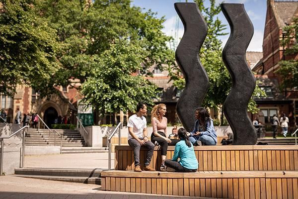 Students sitting near the Sign for Art sculpture on campus