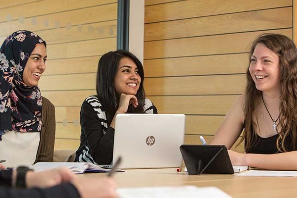 Three students working around a table using laptops and tablets