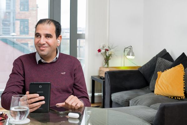 A man sat at a table using a tablet with ear buds.