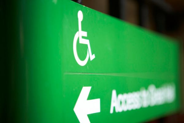 A green sign with a wheelchair user symbol, an arrow and blurred writing