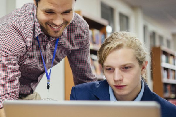 Teacher leans over student as they look at a laptop.