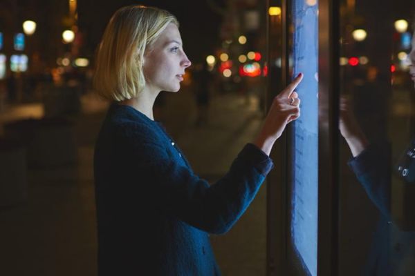 A person stood in a dark street at night pressing a touch screen on a board.