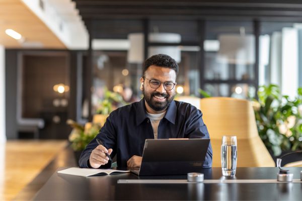 student sat in a cafe working on a laptop and taking notes in a notepad.