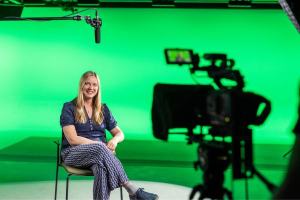 A Leeds University tutor sat on a chair in front of a video camera, with a microphone above their head.