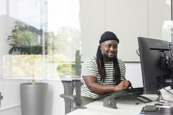 A person sat in an office working at a desktop computer, smiling at the camera.