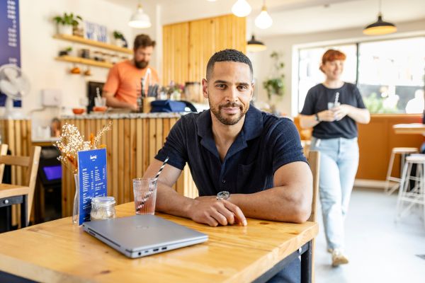 A Masters student sat at a table in a cafe with their laptop on the table.