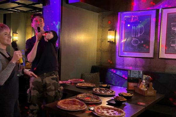 Two mature students smiling and performing karaoke in a bar.