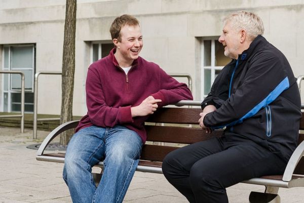 A foundation year student sat on a bench with their mentor. They are smiling and chatting.