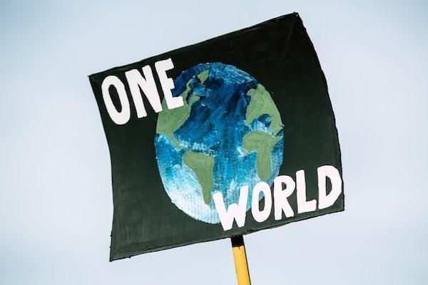 Poster of planet earth against a black background with white text saying "one world", being held in the sky