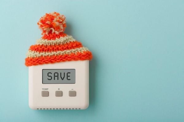Heating thermostat box wearing an orange and yellow striped woolly hat, with SAVE written on the screen