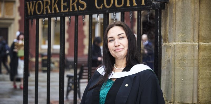 Sarah Lloyd in graduation gowns by the large metal gates of Cloth Workers' Court