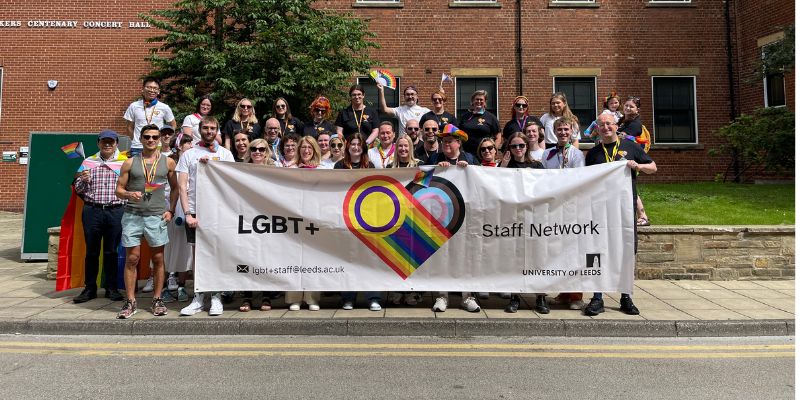 Members of the LGBT+ Staff Network holding the banner and smiling outside of Centenary Hall