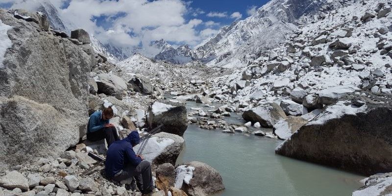 Two researchers sit on the rocks on the bank of a lake.