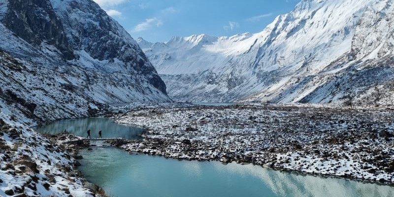 Rivers and lakes, against a snowy mountainous backdrop in Thulagi, Nepal. People are walking across a path over the lake in the distance.