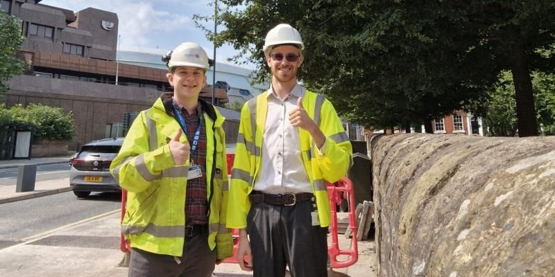 Alex Sutherland stands next to his manager Tom Roebuck in Leeds city centre. Both wear hi vis jackets.