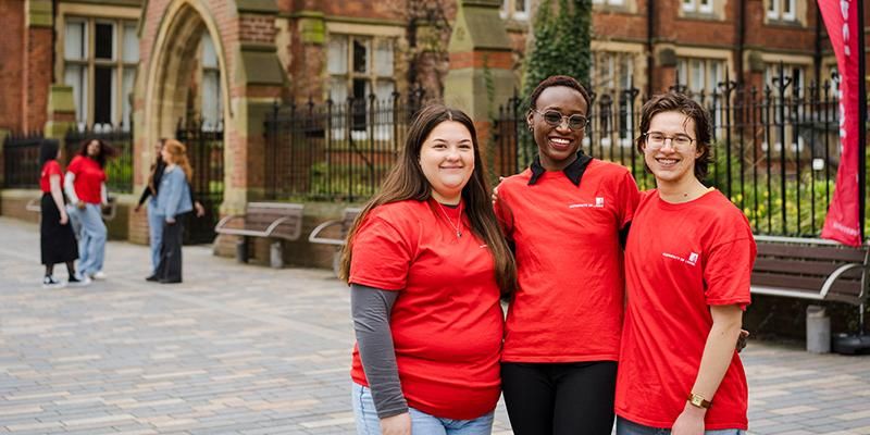 Three smiling student ambassadors in red t-shirts stand together outside  Clothworkers Court.