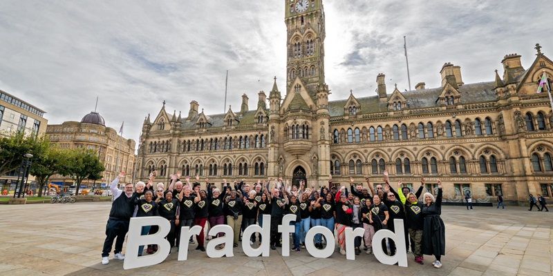 A crowd of people stood in front of Bradford Town hall, cheering and holding up large letters that spell out the word Bradford.