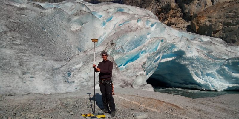 Professor Jonathan Carrivick stands next to a glacier at Nigardsbreen, Norway carrying GPS topographic surveying equipment