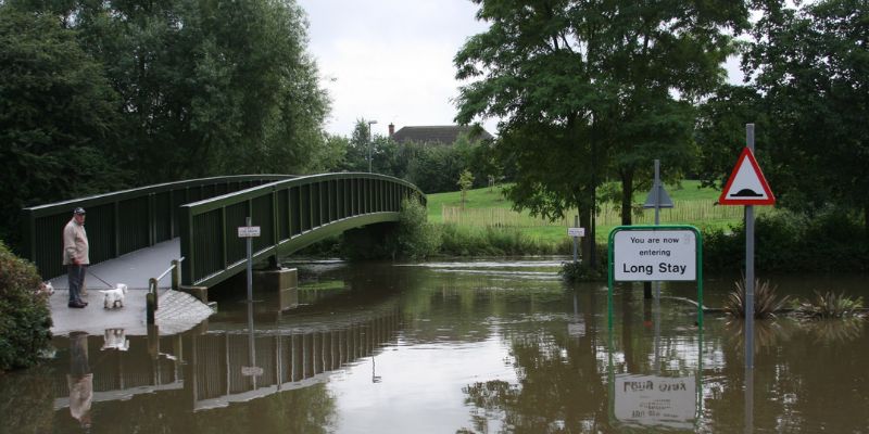 A person and a dog stand on a bridge looking at a flooded car park