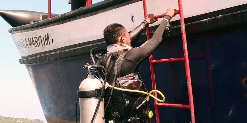 A diver climbing down a ladder on the side of a boat and about to enter the sea.