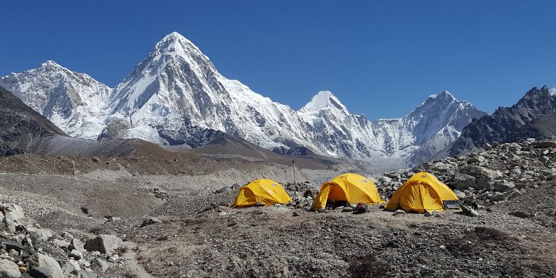 Three yellow tents in a row in bright sunshine on the Khumbu Glacier on Mount Everest with the Himalayan mountain range in the background