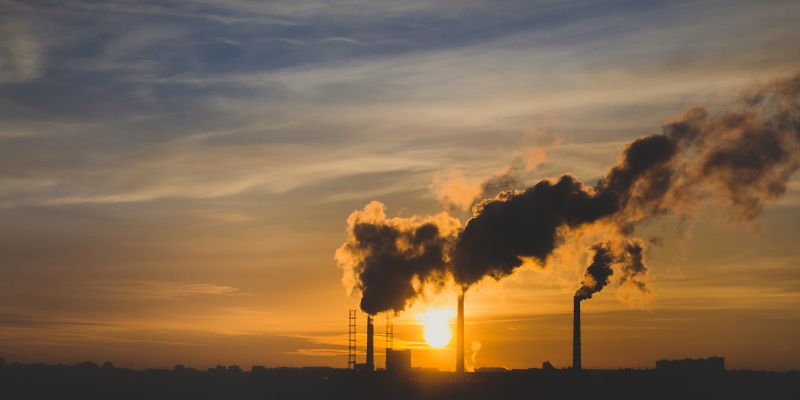 a row of industrial chimneys spewing out smoke into a sky at sunset