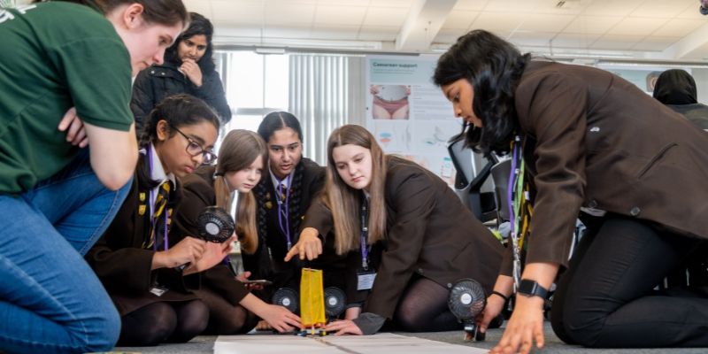 A group of high-school pupils use fans to power a miniature sail boat, on wheels, that they've created.