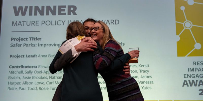 A group of researchers hug on stage after receiving award.