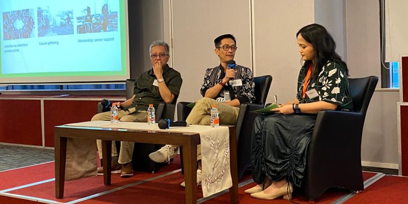 Three speakers sit on stage at an event in conversation with one another