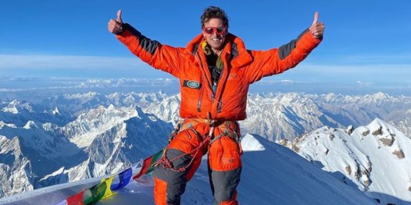 High altitude climber, Kenton Cool on the summit of K2. He is waving and smiling at the camera 