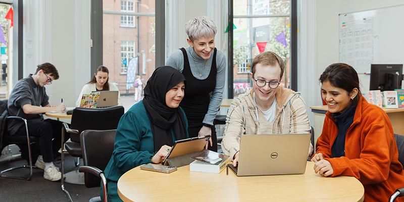 A staff member talking to students working on a laptop in the Lifelong Learning Centre