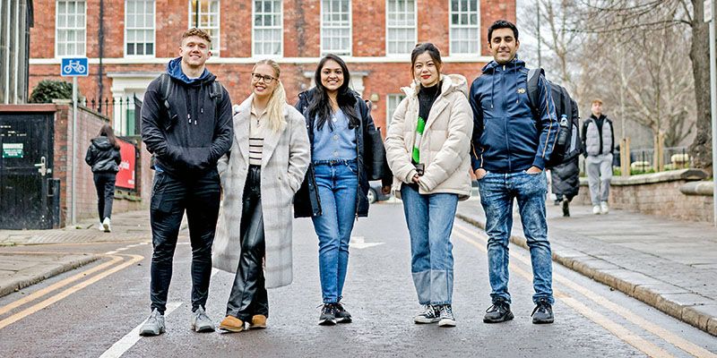 Four students walking down a road on campus at the University of Leeds. A red brick building is behind them.