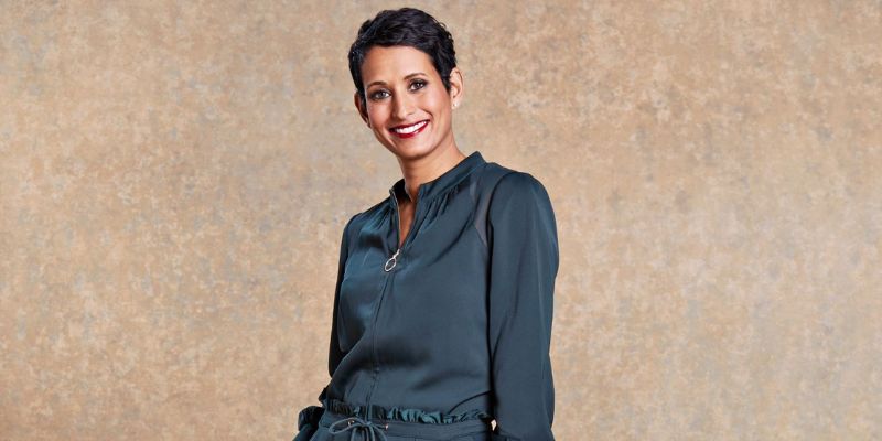 Naga Munchetty, wearing a grey dress, smiles at the camera in front of a beige background