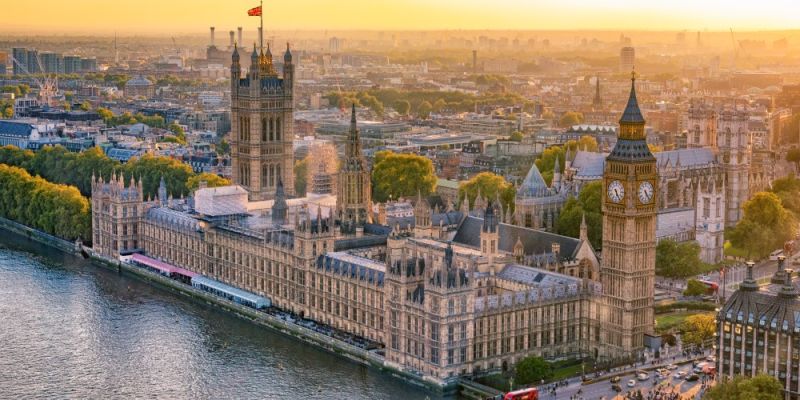 Houses of Parliament with Big Ben tower, next to the river, with the city of London in the background.