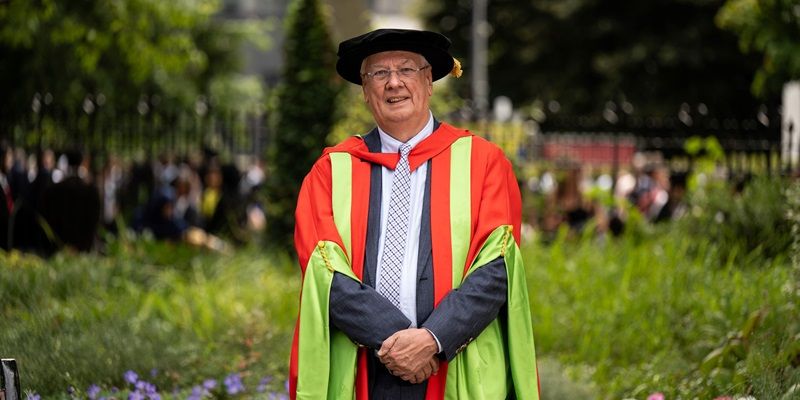 Peter Buckley stood outside on campus on a sunny day wearing a graduation cap and gown.