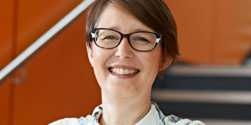 Professor Catherine Johnson wearing a white blouse and glasses smiles directly at the camera.