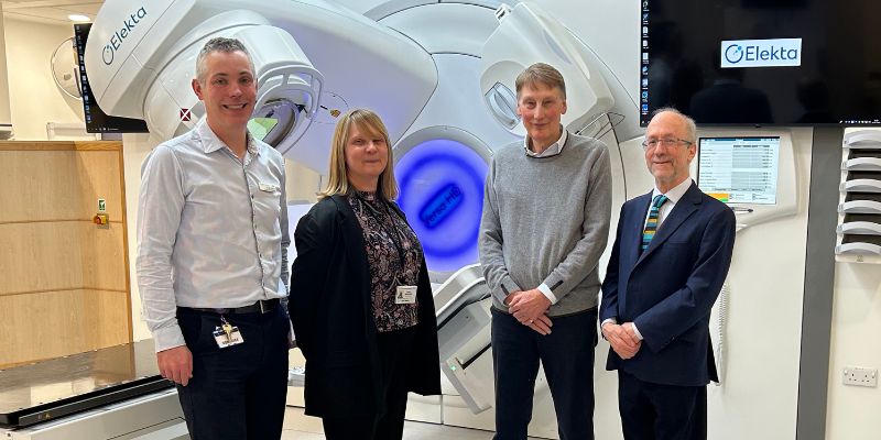 Four people smile in front of  a state-of-the art linear accelerator (LINAC) radiotherapy machine at Leeds Teaching Hospitals NHS Trust. 