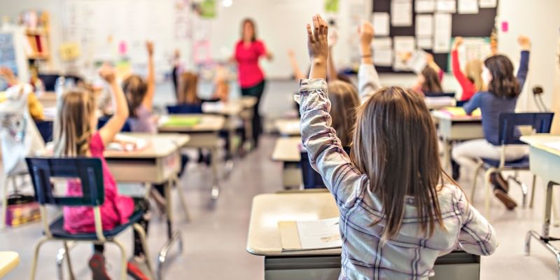 Children seated in a classroom raising their hands