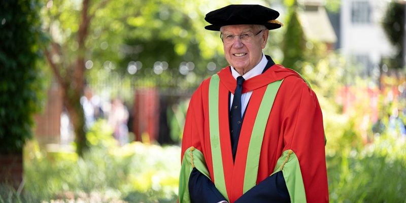 Alan Langlands stood outside on campus on a sunny day wearing graduation cap and gown.