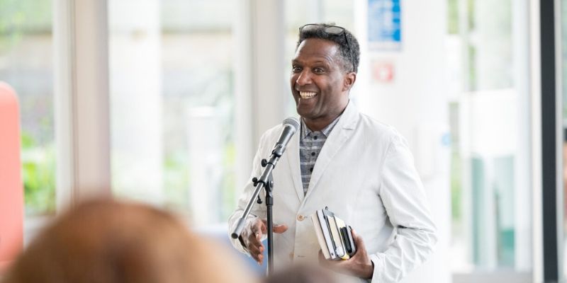 Lemn Sissay OBE FRSL smiles at the audience as he gives a speech