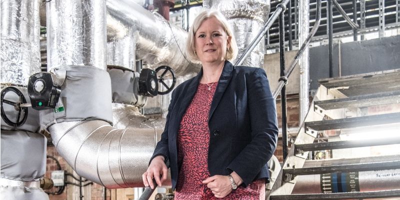 Professor Cath Noakes stands on stairs in front of silver ventilation pipes