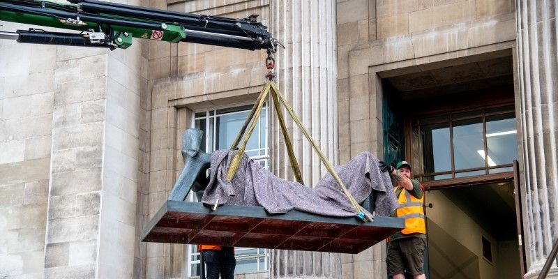 A crane moves Henry Moore's Three Piece Reclining Figure No.2: Bridge Prop. The photo is taken outside the Parkinson building. 