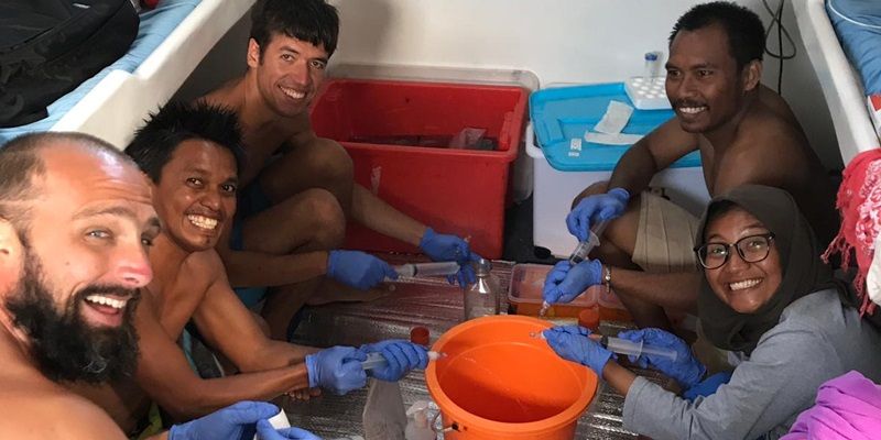 A smiling group of researchers on board a boat with equipment for taking samples.