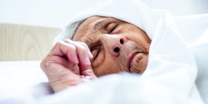 An elderly person wearing a headscarf, ill in bed