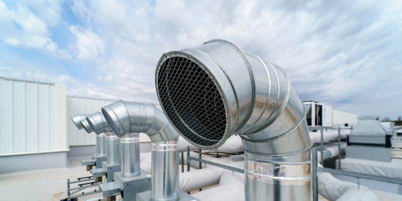 Silver ventilation pipes on rooftop, against backdrop of blue sky