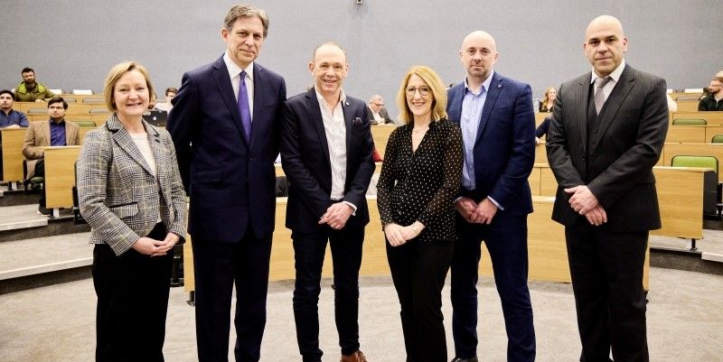 A group of people stood in the lecture theatre smiling at the camera. 