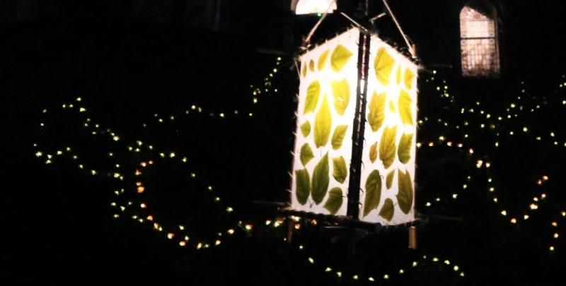 A leaf lantern hangs from a tree with fairy lights in the background.