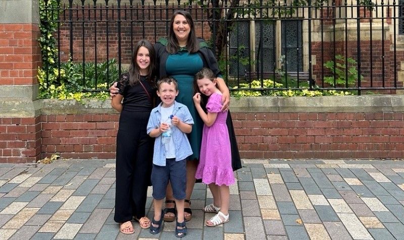 Graduate Emily Tennant with her three children stood outside the Great Hall smiling at the camera