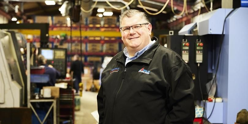 A smiling person stood in an industrial building with manufacturing equipment